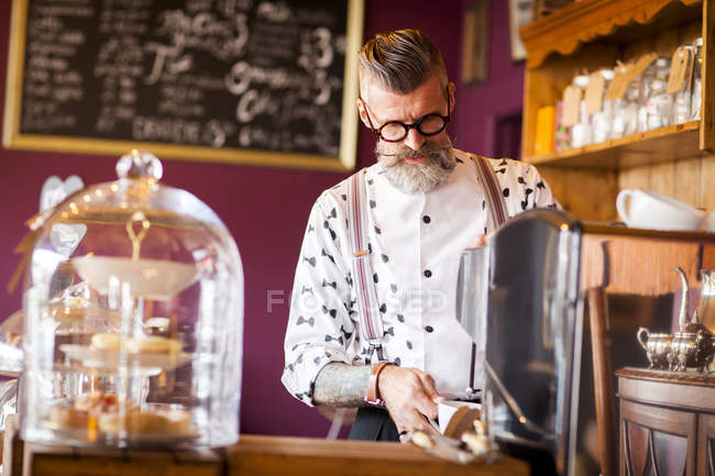 Quirky vintage senior man using coffee machine in tea room — Stock Photo