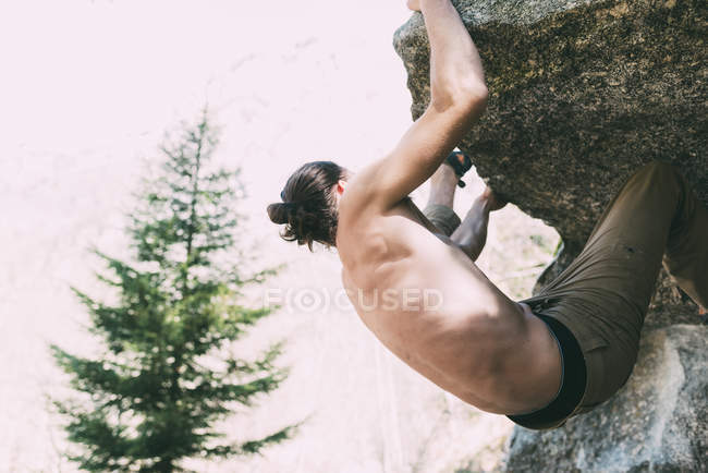 Bare chested male climbing on large boulder — Stock Photo