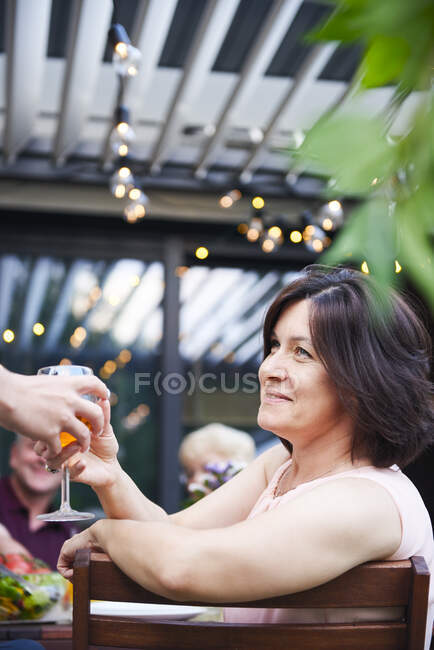 Madura mujer consiguiendo a mano vino en familia almuerzo en patio mesa - foto de stock