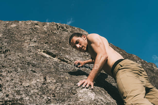 Bare chested young male climbing on boulder — Stock Photo