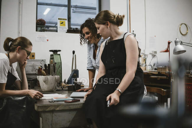Drei Juwelierinnen betrachten Skizzenblock bei Werkbank-Treffen — Stockfoto