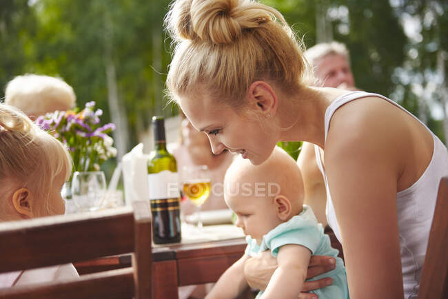 Mujer joven con bebé e hijas pequeñas en la mesa del patio almuerzo familiar - foto de stock