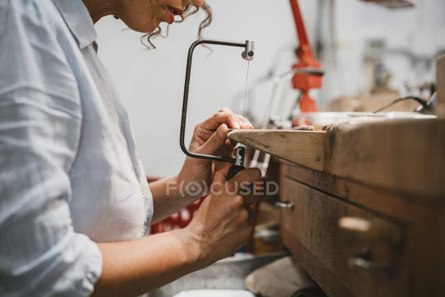 Cropped view of female jeweler using coping saw at workbench — Stock Photo