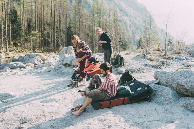 Adult bouldering friends taking off trainers at riverside, Lombardy, Italy — Stock Photo