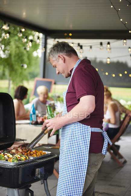 Mature man barbecuing on patio at family lunch — Stock Photo