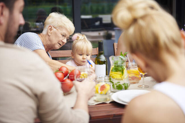 Mujer mayor con nieta pequeña en el almuerzo familiar en la mesa del patio - foto de stock