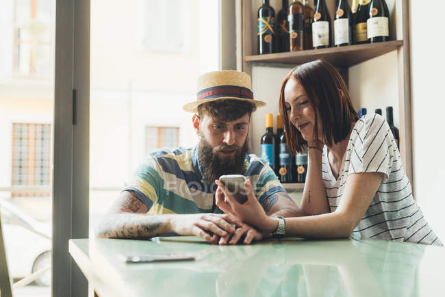 Пара, которая смотрит на смартфон за барным столом — стоковое фото
