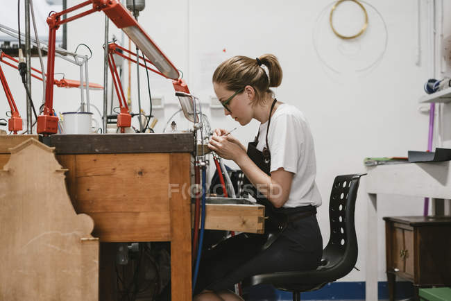 Вид збоку Жіночий ювелір, що працює з мініатюрним ручним інструментом на верстаті — стокове фото