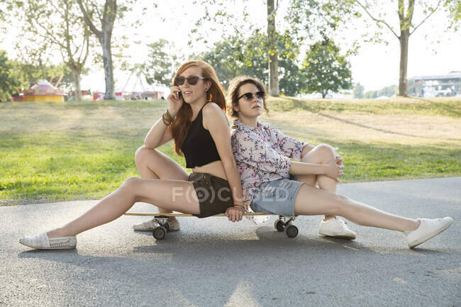 Porträt zweier junger Frauen im Freien, die auf einem Skateboard sitzen — Stockfoto