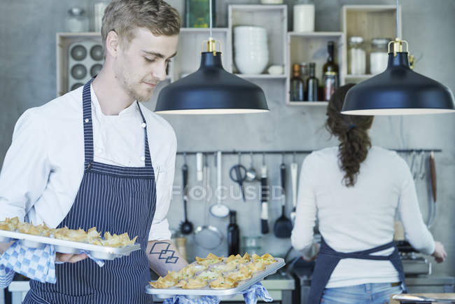 Chef in kitchen holding baking trays of canapes — Stock Photo