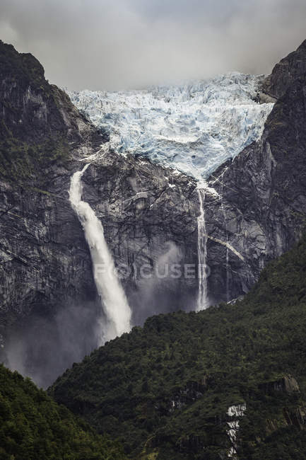 Cascada que fluye desde el glaciar al borde de la cara de roca montañosa, Parque Nacional Queulat, Chile - foto de stock