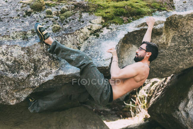 Bare chest male boulderer climbing boulder overhang, Lombardía, Italia - foto de stock