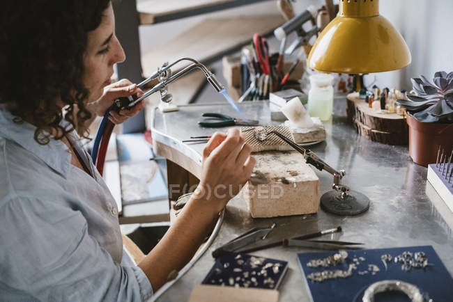 Female jeweler using blow torch at workbench — Stock Photo