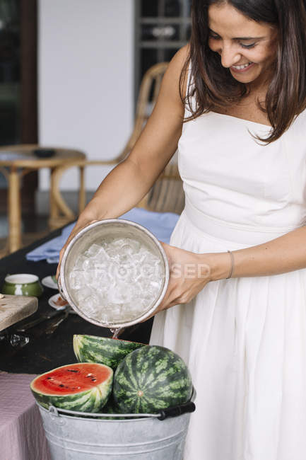 Woman pouring ice water into bucket of watermelon — Stock Photo