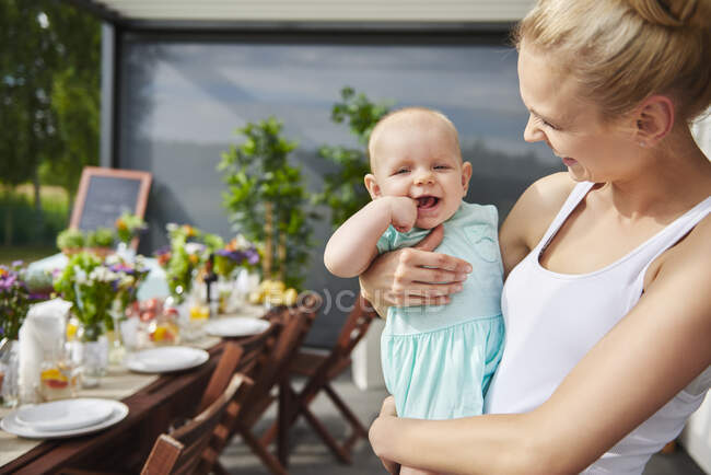 Young woman carrying baby daughter at family lunch by patio table — Stock Photo