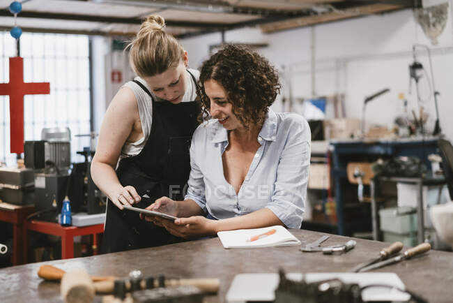 Two female jewellers looking at digital tablet at workbench — Stock Photo