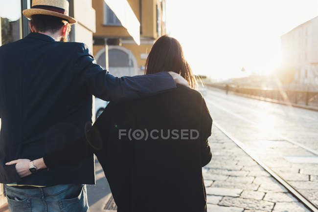 Visão traseira do casal passeando ao longo da calçada iluminada pelo sol — Fotografia de Stock