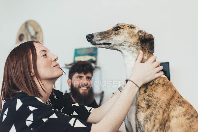 Jeune femme avec petit ami caressant chien dans l'appartement — Photo de stock