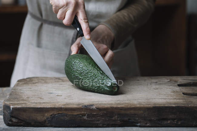 Mulher cortando abacate na tábua de corte, seção meio — Fotografia de Stock