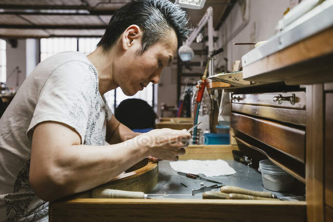 Homme bijoutier inspectant le métal à l'établi — Photo de stock