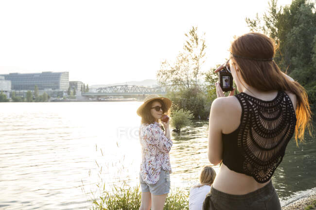 Tres amigas en el borde del agua, una joven fotografiando amigas - foto de stock