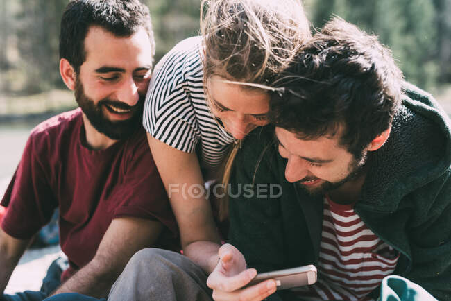 Три молодых взрослых друга смотрят и смеются над смартфоном, Ломбардия, Италия — стоковое фото