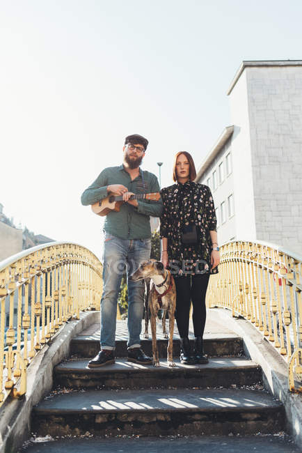 Portrait of cool couple with dog standing on footbridge — Stock Photo