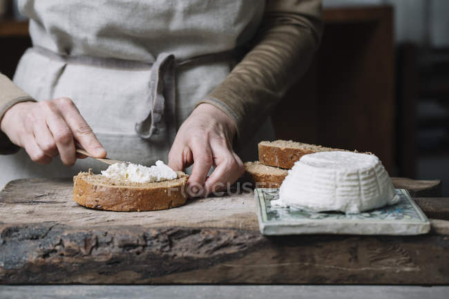 Femme étalant du fromage ricotta sur une tranche de pain, section médiane — Photo de stock