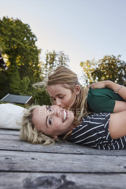 Madre e hija tumbadas en una terraza de madera al aire libre - foto de stock