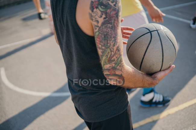 Cropped view of friends on basketball court holding basketball — Stock Photo