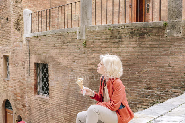 Turista femenina madura sentada en la escalera y comiendo helado en Siena, Toscana, Italia - foto de stock