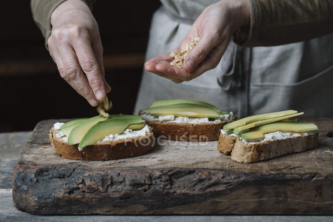 Woman sprinkling chopped walnuts onto avocado bruschetta, mid section — Stock Photo