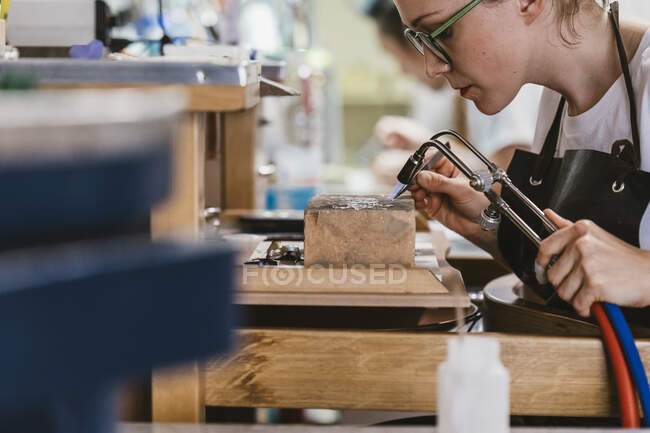 Female jeweller using blow torch at workbench — Stock Photo