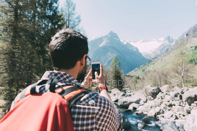 Veduta posteriore dell'escursionista maschio che fotografa il fiume di montagna, Lombardia, Italia — Foto stock