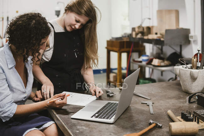 Zwei Juwelierinnen zeichnen Notizblock an Werkbank — Stockfoto