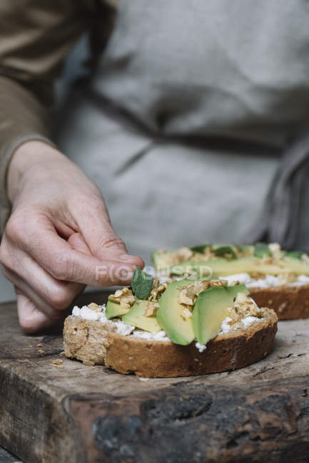 Woman placing herbs on ricotta, avocado and walnut bruschetta, close-up — Stock Photo