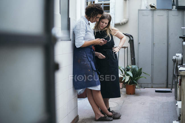 Дві жінки-ювеліри дивляться на смартфон у ювелірній майстерні — стокове фото
