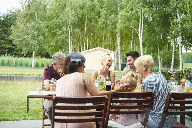 Три поколения семьи обедают на обеденном столе во дворе — стоковое фото