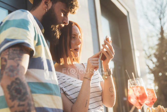 Casal usando tela sensível ao toque do smartphone no café da calçada — Fotografia de Stock