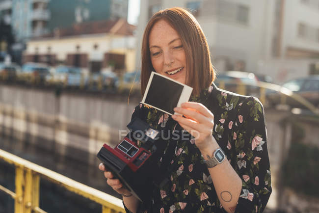 Young woman looking at instant photo by canal — Stock Photo
