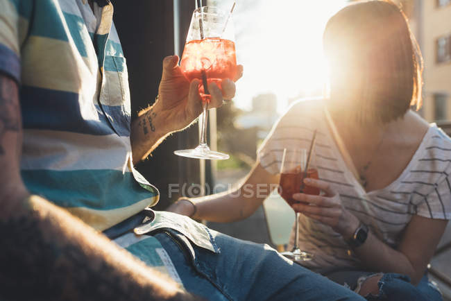 Recortado disparo de pareja sentado fuera de la acera iluminada por el sol café tomando cócteles - foto de stock