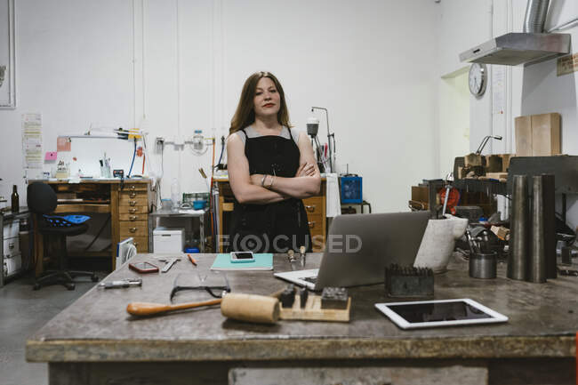 Portrait of female jeweller with arms folded in jewellery workshop — Stock Photo