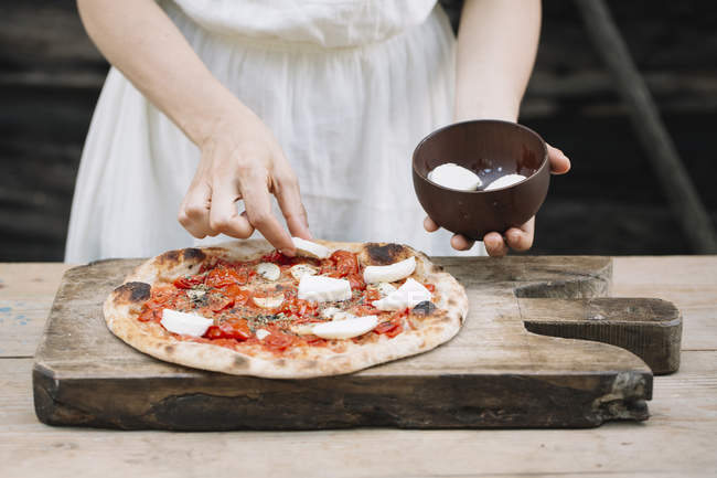 Imagen recortada de Mujer poniendo mozzarella en pizza casera - foto de stock