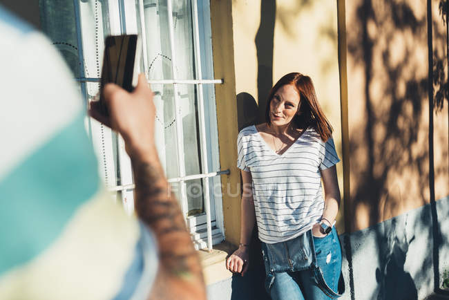 Sobre hombro vista de hombre fotografiando novia inclinada contra casa - foto de stock
