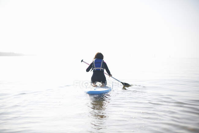 Rear view of female paddleboarder paddling out on misty sea — Stock Photo