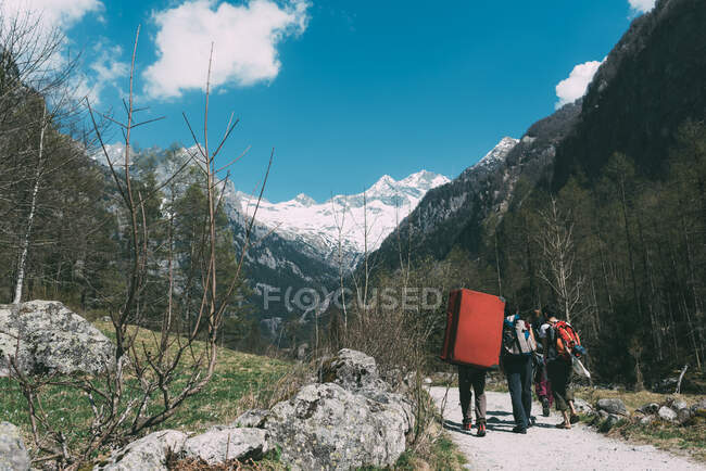 Vista trasera de amigos adultos con mochila de bouldering mat caminando a lo largo de la carretera rural, Lombardía, Italia - foto de stock