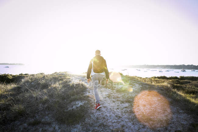 Вид сзади на молодого человека, идущего вдоль песчаных дюн — стоковое фото