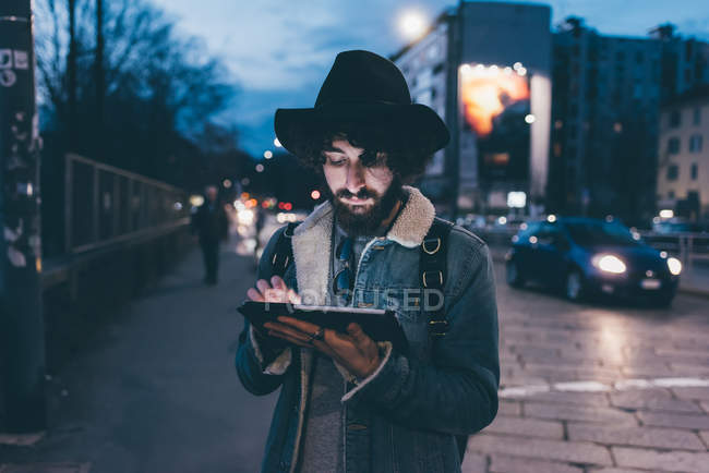 Junger Mann steht in der Abenddämmerung mit digitalem Tablet auf der Straße — Stockfoto