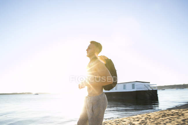 Young man with backpack on sunlit beach — Stock Photo