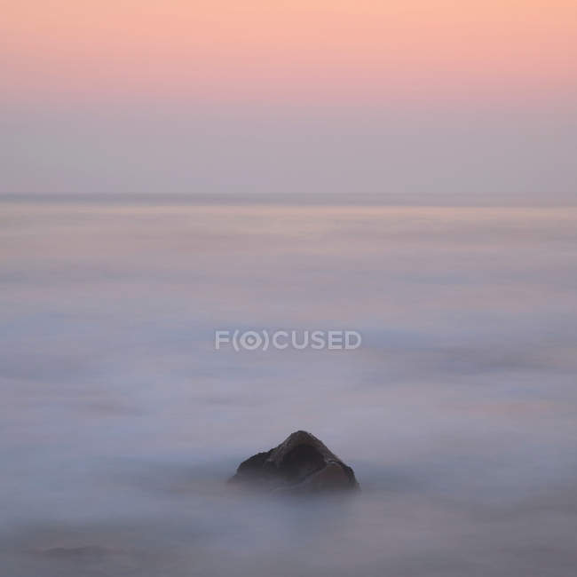 Una roca en el mar brumoso al amanecer - foto de stock
